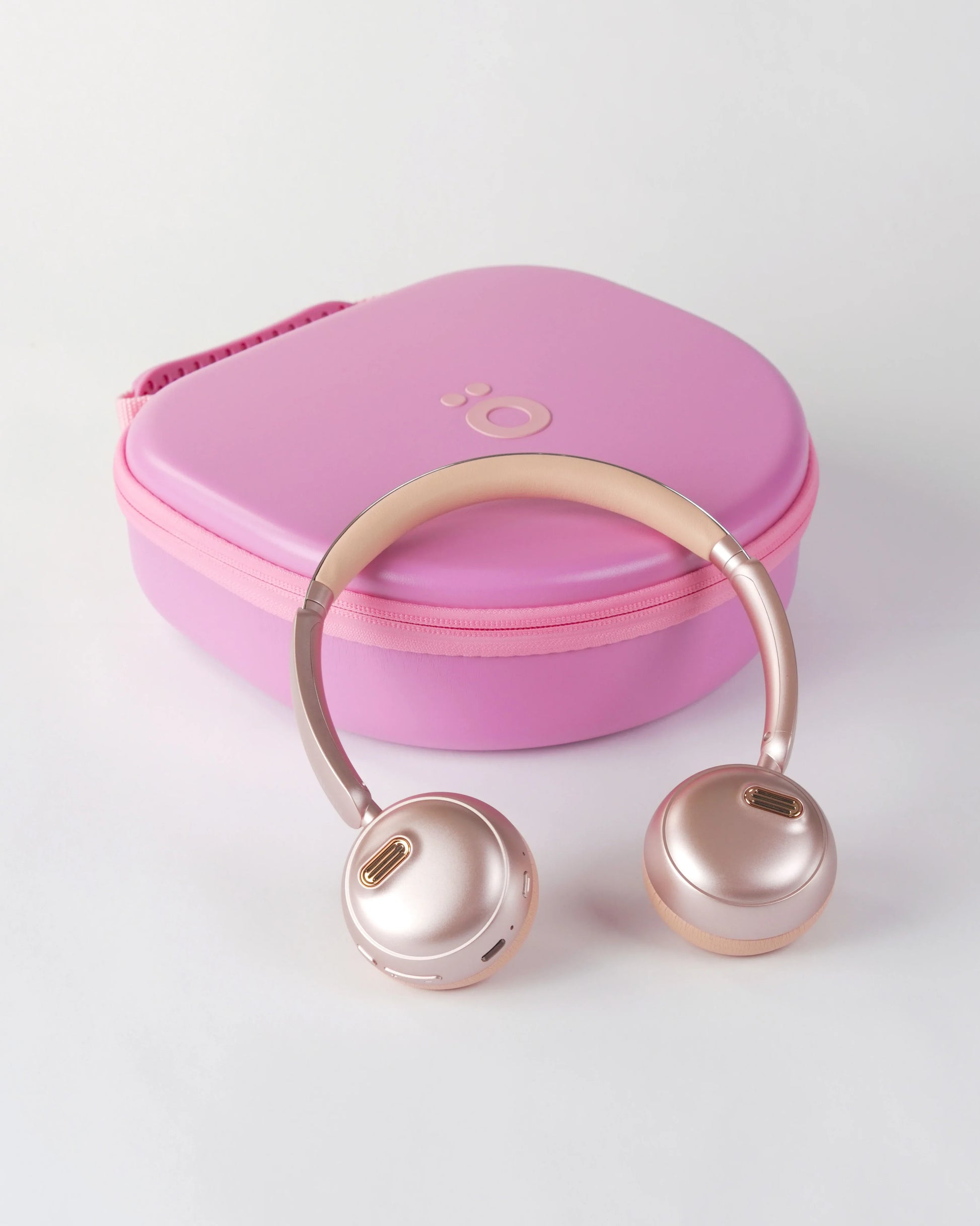 Rose gold höhen aura mini on-ear headphones placed in front of their circular pink hardshell carrying case with the höhen logo
