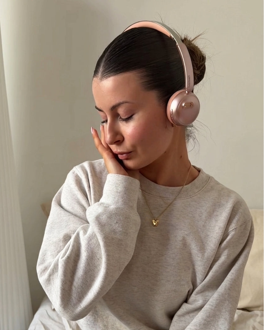 A portrait of a woman wearing the rose gold höhen Aura Mini wireless headphones, reflecting a moment of calm and sophisticated technology use