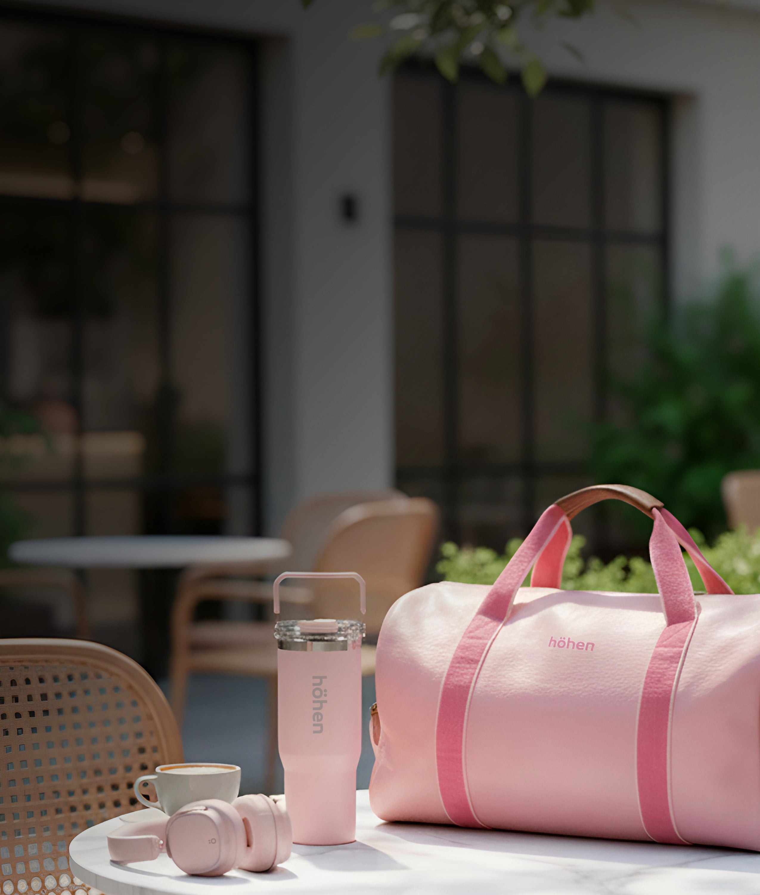 A collection of höhen products on a table: Aura Pro headphones, Essential Tumbler, and One bag, all in pastel pink.