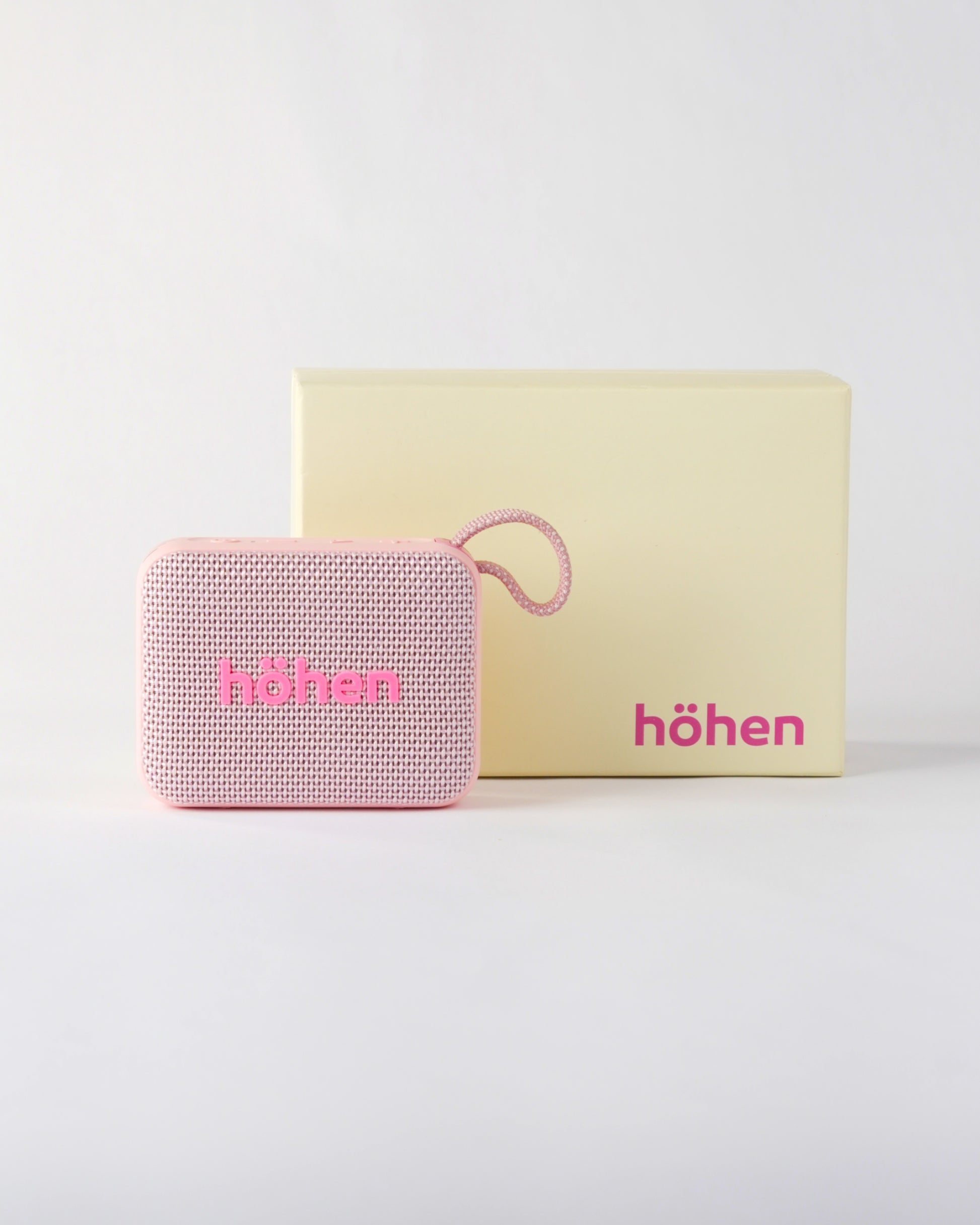 The pink höhen move bluetooth speaker presented next to its premium minimalist cream-colored branded packaging box
