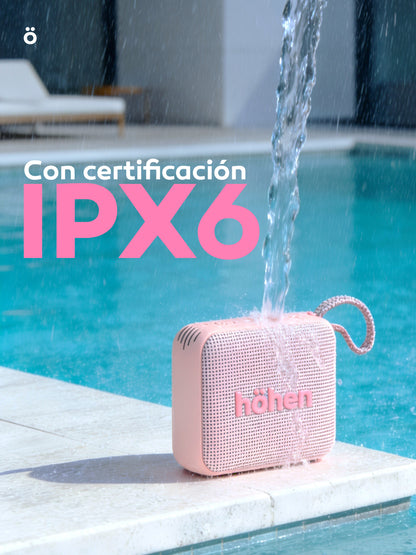 The pink höhen move portable bluetooth speaker sitting by a pool with water splashing over it, highlighting its IPX6 waterproof certification banner.