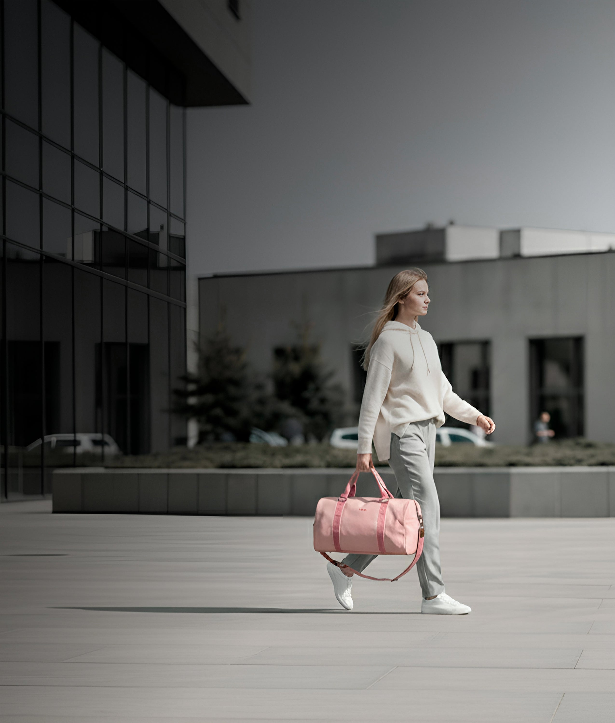 Woman walking through the city carrying the höhen one duffel bag in pink, perfect for an active urban lifestyle.
