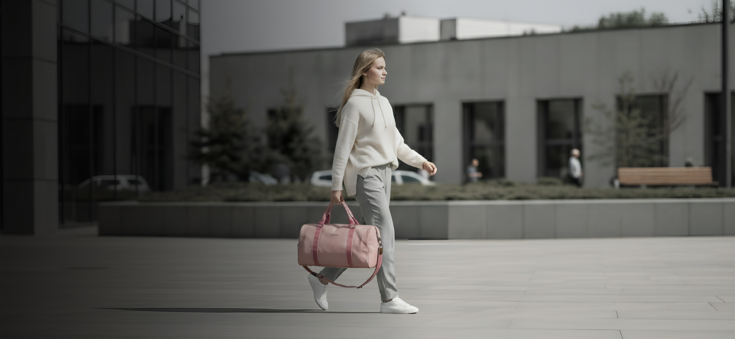 Woman walking through the city carrying the höhen one duffel bag in pink, perfect for an active urban lifestyle.