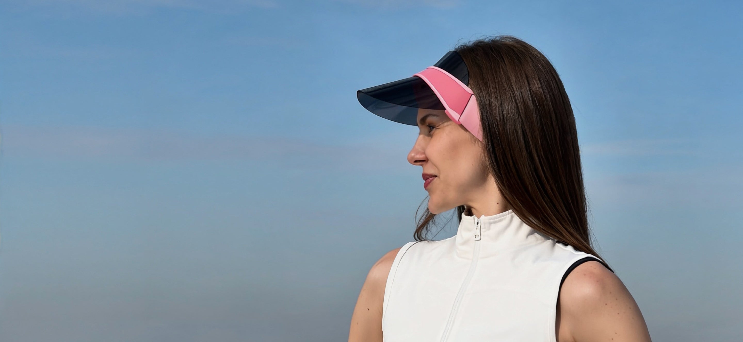 Woman wearing the pink höhen Soleil visor outdoors against a blue sky, featuring a lightweight sporty design with sun protection and modern style.