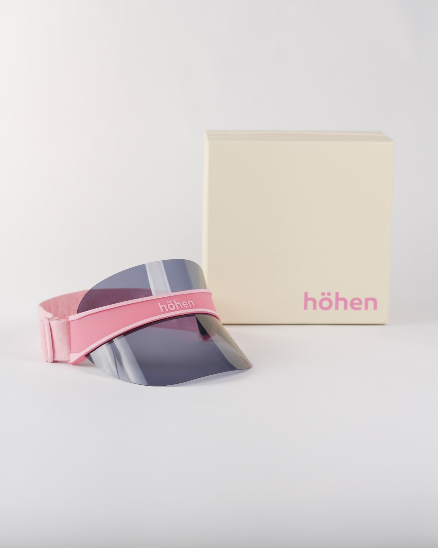 Studio shot of the höhen soleil women’s sports visor in pink featuring a dark tinted smoke lens for sun protection, including the premium höhen branded packaging.