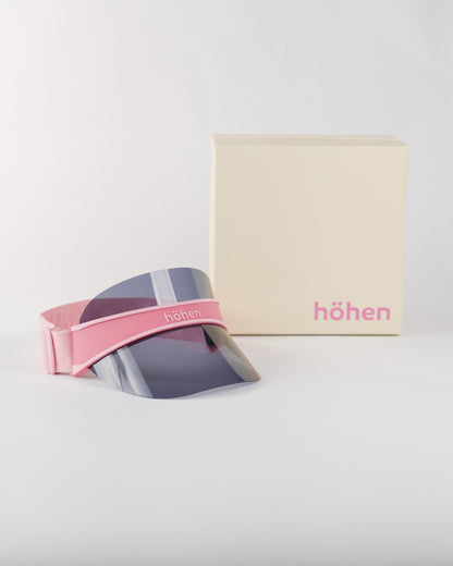 Studio shot of the höhen soleil women’s sports visor in pink featuring a dark tinted smoke lens for sun protection, including the premium höhen branded packaging.