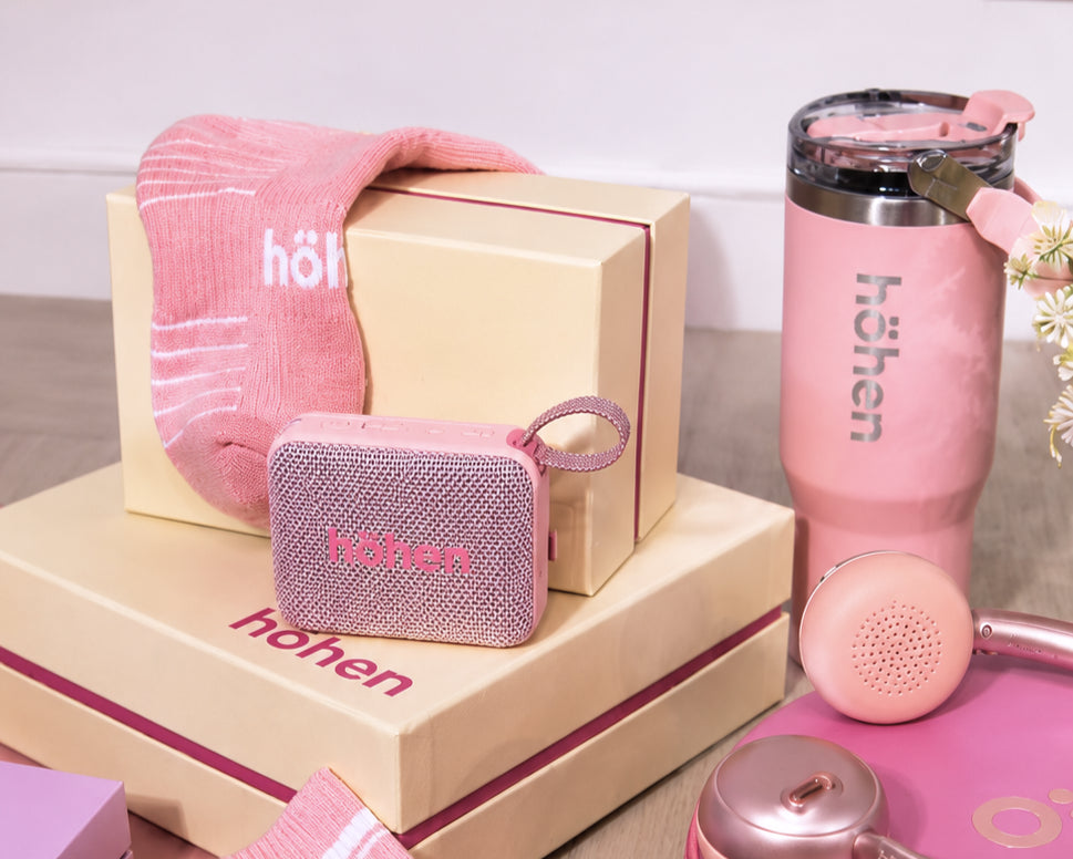 Pink höhen lifestyle essentials featuring the Aura Mini headphones, Move mini speaker, Core Merino socks, and insulated tumbler arranged in a soft aesthetic setup with branded packaging.
