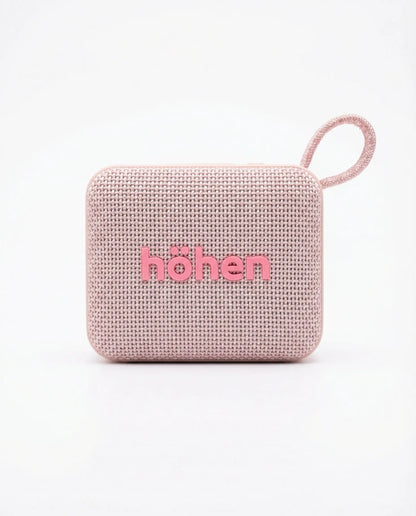 Parlante Bluetooth Höhen Move color rosa con acabado en tela, diseño compacto y correa de transporte.