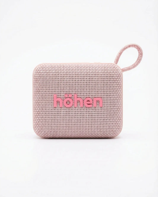 Parlante Bluetooth Höhen Move color rosa con acabado en tela, diseño compacto y correa de transporte.