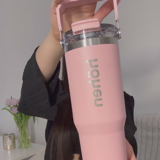 A close-up video of a woman holding and showing the pink höhen Essential tumbler, highlighting its sleek design and the vertical brand logo in a clean, sophisticated setting.