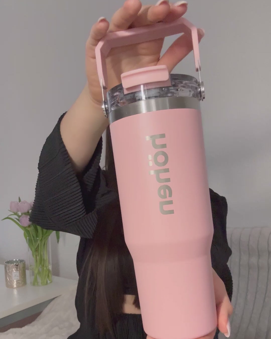 A close-up video of a woman holding and showing the pink höhen Essential tumbler, highlighting its sleek design and the vertical brand logo in a clean, sophisticated setting.