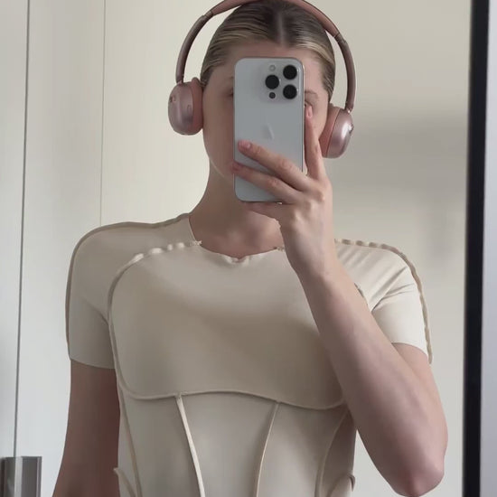 A woman wearing pink höhen aura mini wireless headphones during a workout session, showing a mirror selfie and the back detail of the headphones with a sleek bun hairstyle.