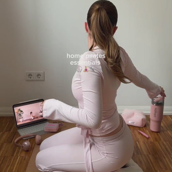 A lifestyle video showing a woman sitting on a yoga mat with her "home pilates essentials," including the pink höhen Essential tumbler, the Aura Mini headphones in rose gold, and the Move portable speaker.
