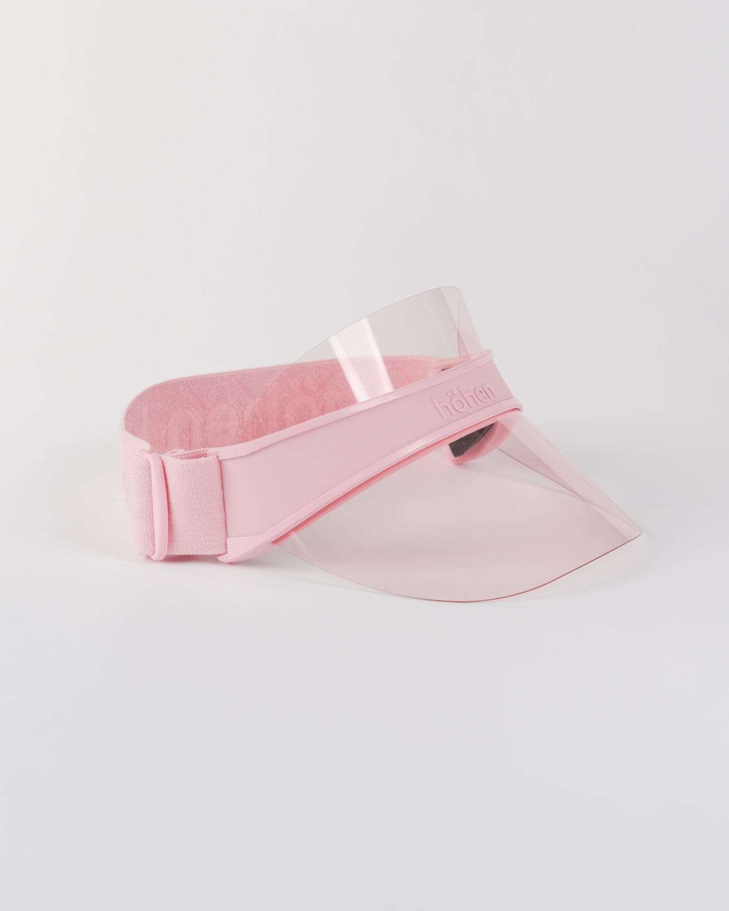 Side view of a pink höhen soleil women’s sports visor with a clear pink transparent shield and adjustable elastic band on a white background.